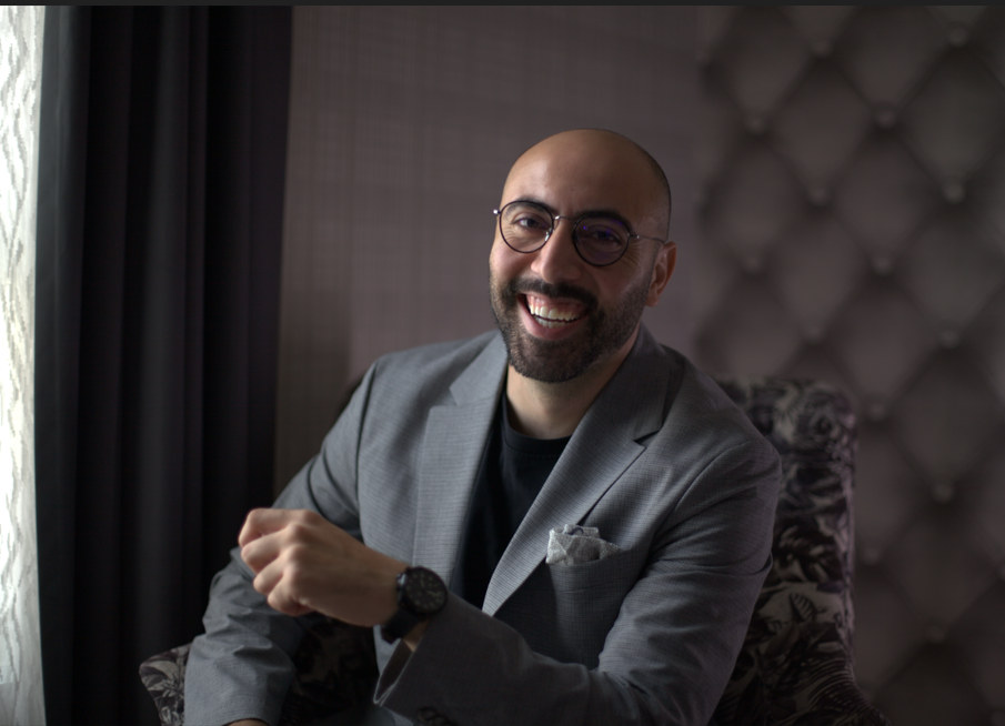 Ali Al Mokdad, seated and smiling, wearing glasses
